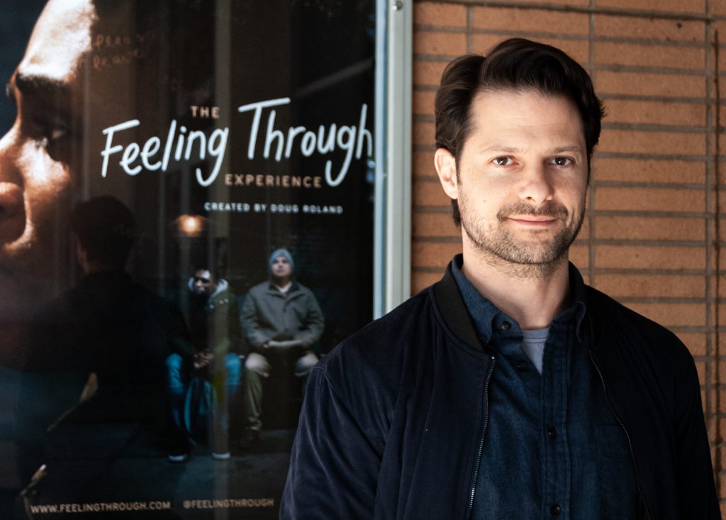 Headshot of film maker, Doug Roland, in front of a poster of his film Feeling Through