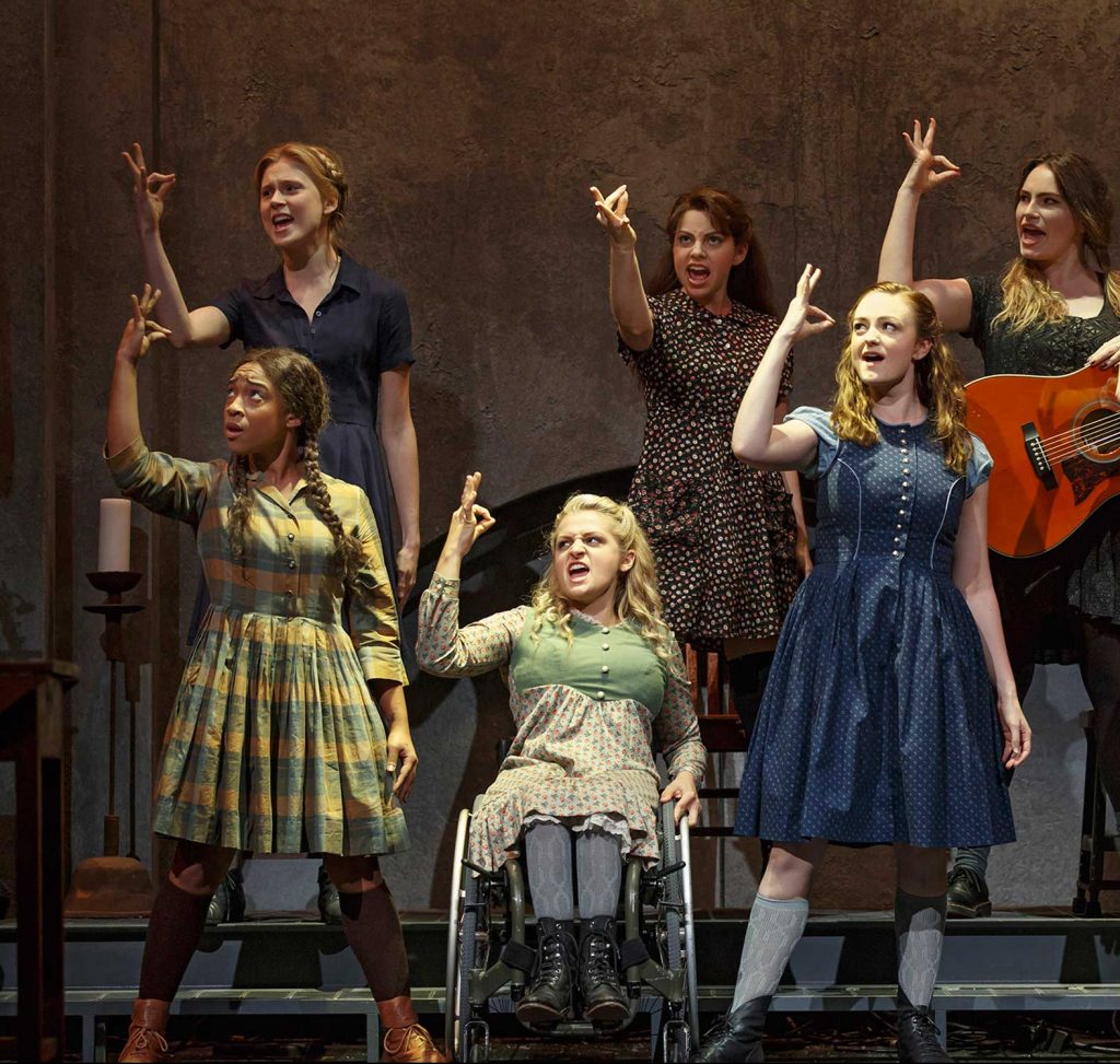 Photo of the six actors in Deaf West's production of Spring Awakening. The actors are all signing using ASL. One actor holds a guitar. Another actor is using a wheelchair.