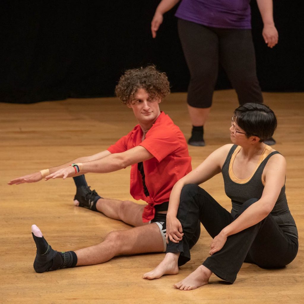Image of two dancers sitting on the floor of a dance studio.
