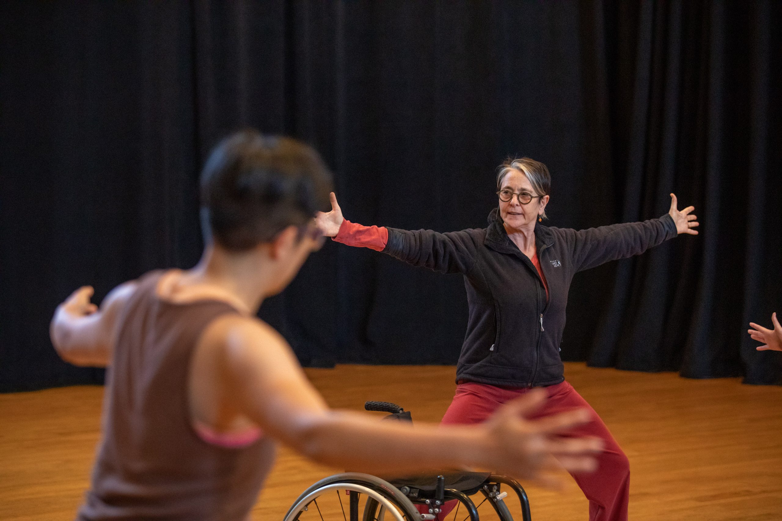 Victoria Marks demonstrates a movement during the 2019 Dancing Disability Workshop. Her arms are outstretched and knees slightly bent.