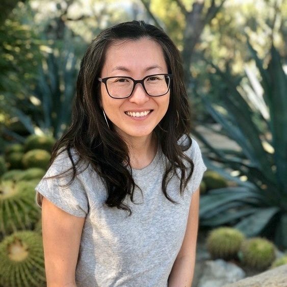 A Korean woman with dark hair and glasses smiles against a background of succulents and plants.