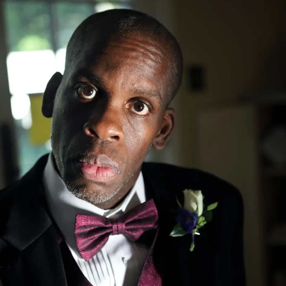 Headshot of Leroy Moore Jr., a Black man wearing a black suit with a plum bowtie.