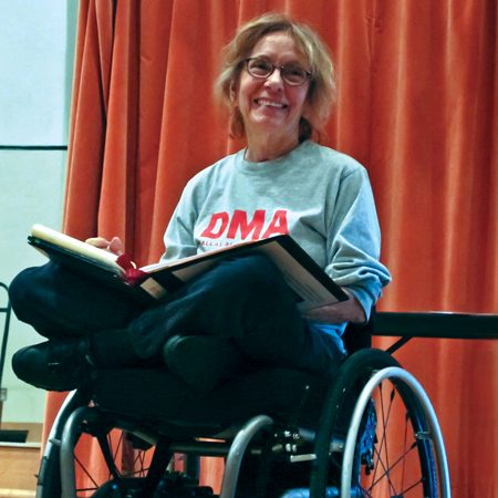 Professor Lewis, a white woman with mid-length blonde hair, smiles toward the camera in her wheelchair.