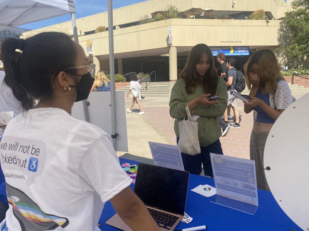 Ruanne, a member of the SoMAA research team, stands masked behind the SoMAA booth at UCLA's Deaf Awareness Fair as students who were enticed with prizes, take the social media accessibility survey.