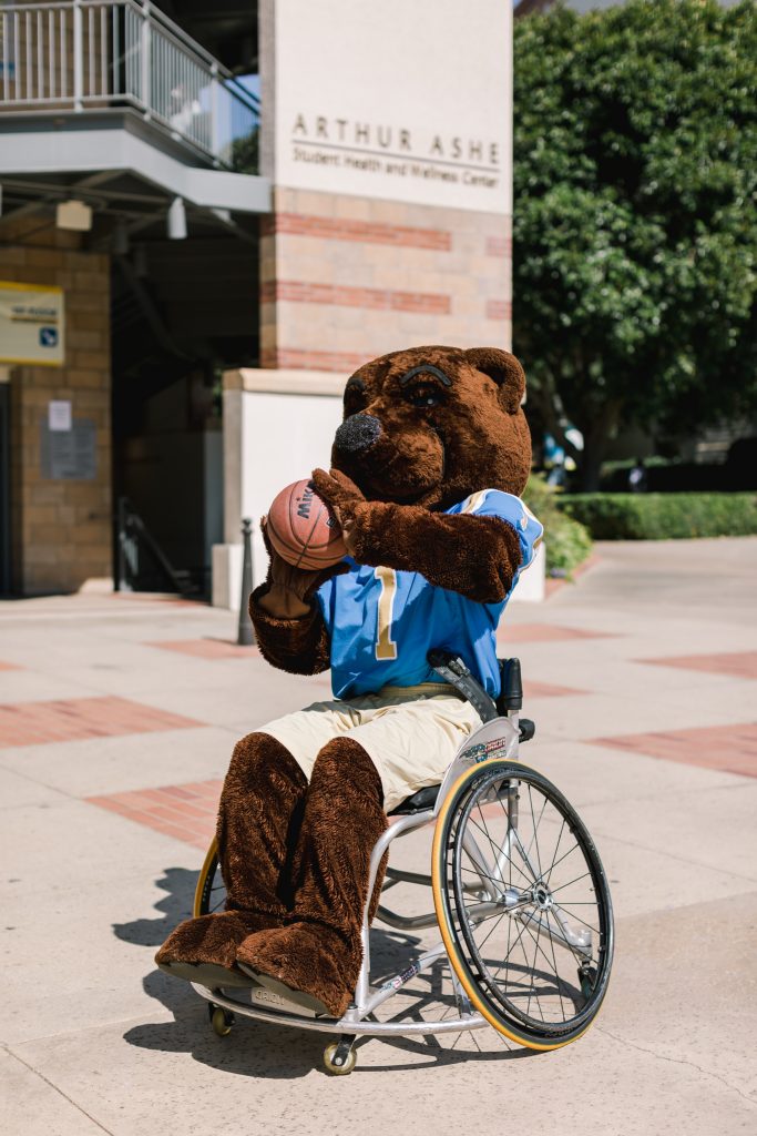 Photo of Joe Bruin in a wheelchair readying to shoot the basketball. Photo credit: TiffanyJPhotography