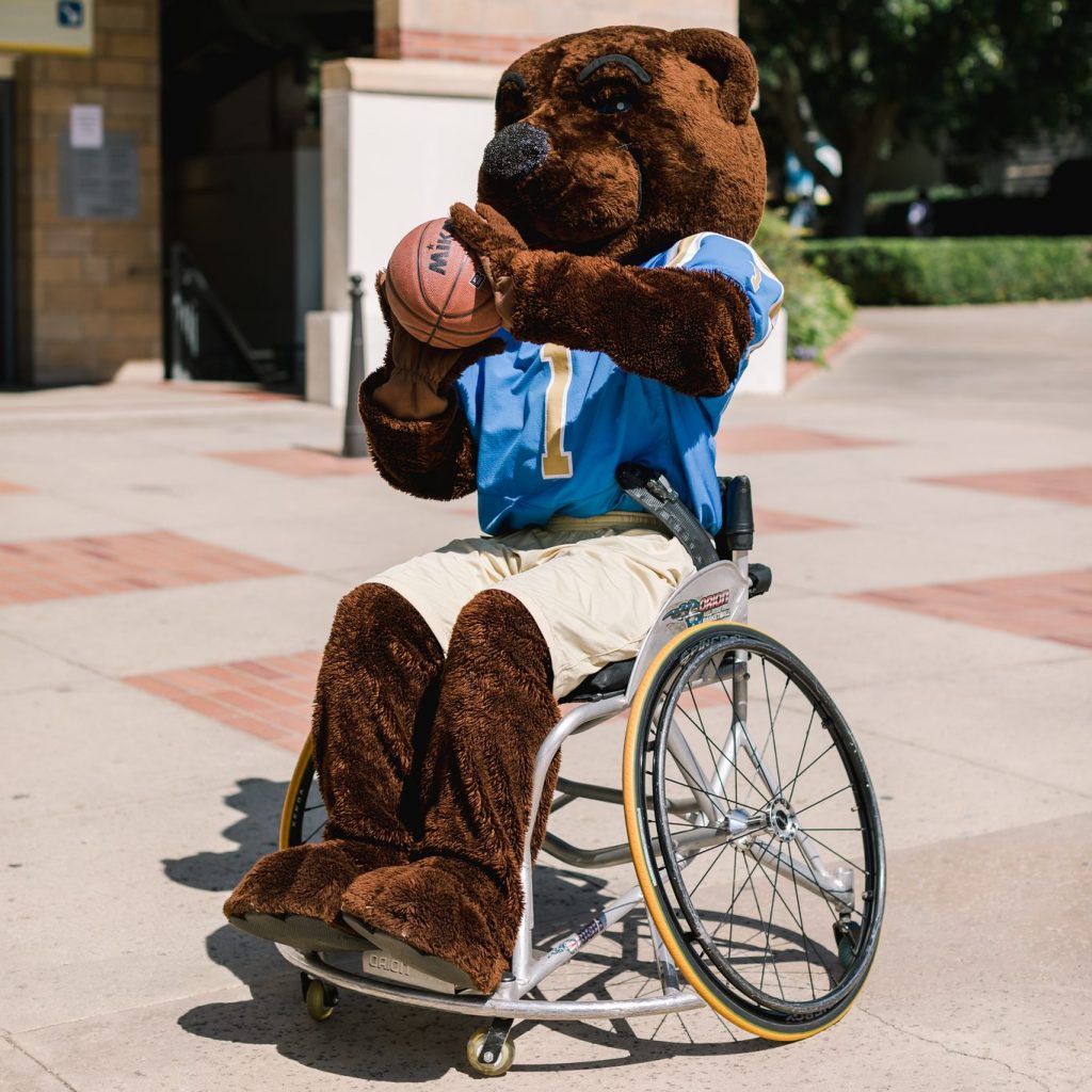 Image of Joe Bruin mascot in a wheelchair readying to throw a basketball. Photo credit: TiffanyJPhotography