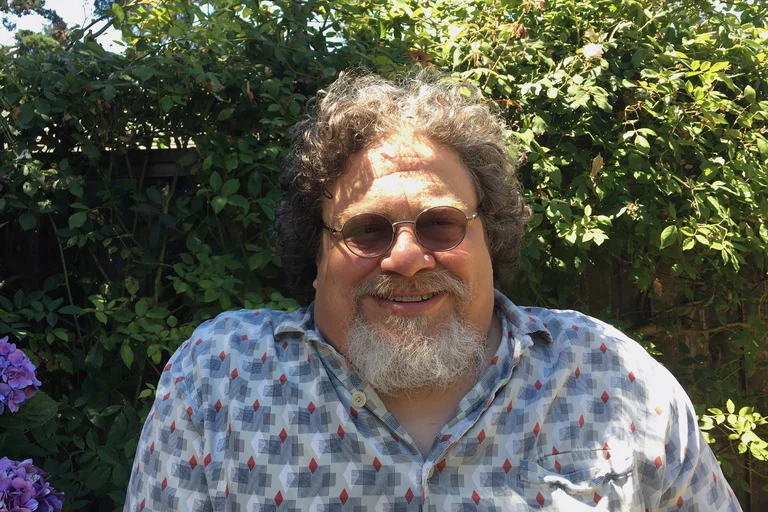 A headshot of Jim LeBrecht smiling and standing in front of trees.