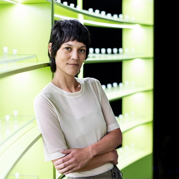 Chinese-American woman with short dark hair leans against a display of saliva vials, arms crossed