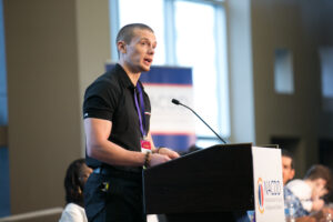 Russell Lehmann in a black polo standing and speaking from a podium.