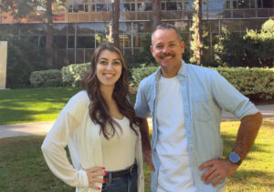 Mariam Janvelyan (left) in white top and Benjamin Lewis in blue and white top stand outside with hands on their hips.