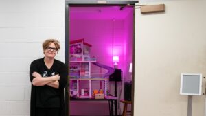 Jenny Olivia Johnson poses to the side of a doorway that opens into a room with an immersive light and music installation called "Dream House" by La Monte Young.