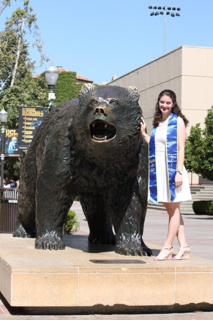 Graduate poses in front of the Bruin Bear.