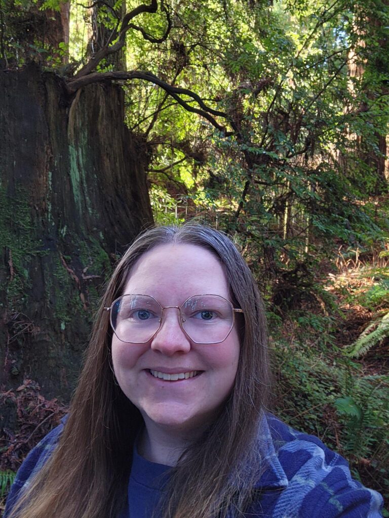 Woman poses in front of trees.